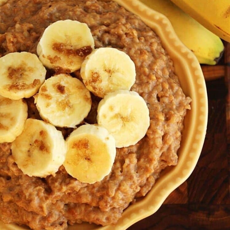 Overhead image of a yellow bowl of crock pot peanut butter banana oatmeal topped with banana slices next to a bunch of bananas