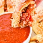 Hand dipping a piece of pizza ring into pizza sauce in bowl