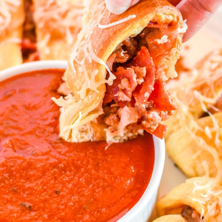 Hand dipping a piece of pizza ring into pizza sauce in bowl