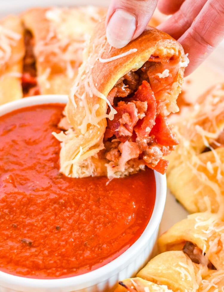 Hand dipping a piece of pizza ring into pizza sauce in bowl