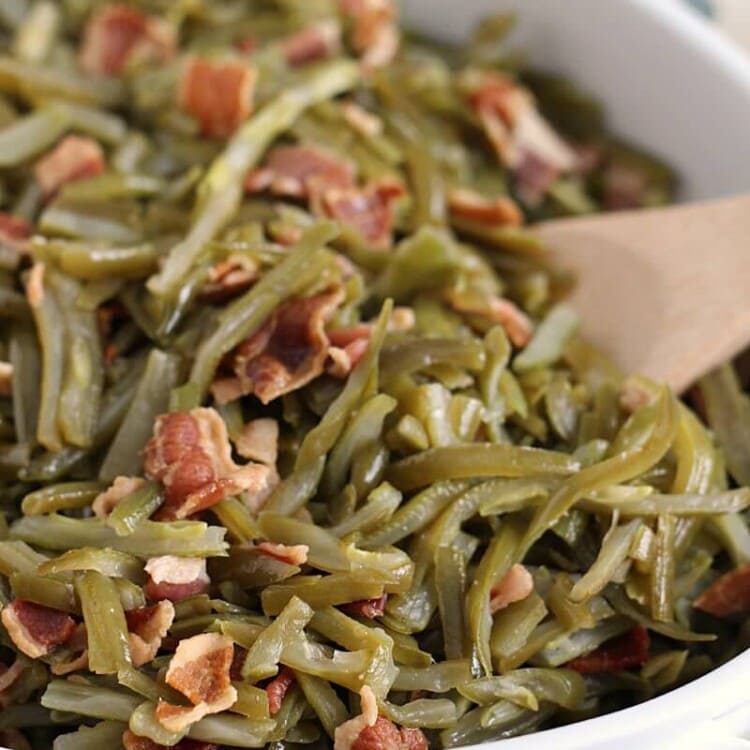 Crock pot bacon green beans in a white baking dish with a wooden spoon