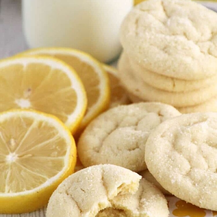Lemon sugar cookies stacked on a yellow bag along with lemon slices and a glass of milk