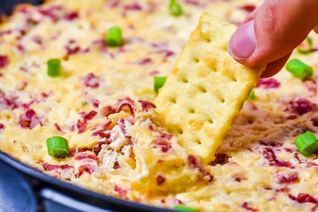 Cracker scooping baked reuben dip out of cast iron skillet