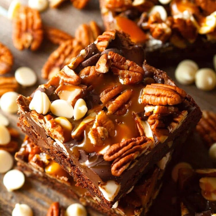 Stack of turtle brownies on a table with pecans and white chocolate chips