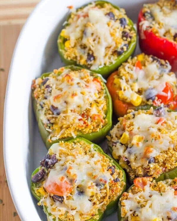 Tex mex quinoa stuffed peppers topped with shredded cheese in a white baking dish