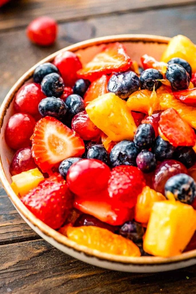 fruit salad of strawberries, blueberries, red grapes, pineapple and orange in a white bowl