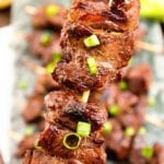 Up close image of an Asian steak kebab being held over a tray of more Asian steak kebabs