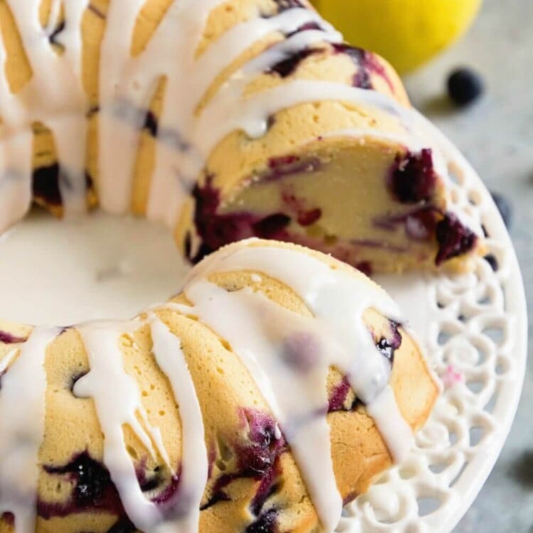Blueberry lemon pound cake drizzled with icing on a white cake stand with a slice missing