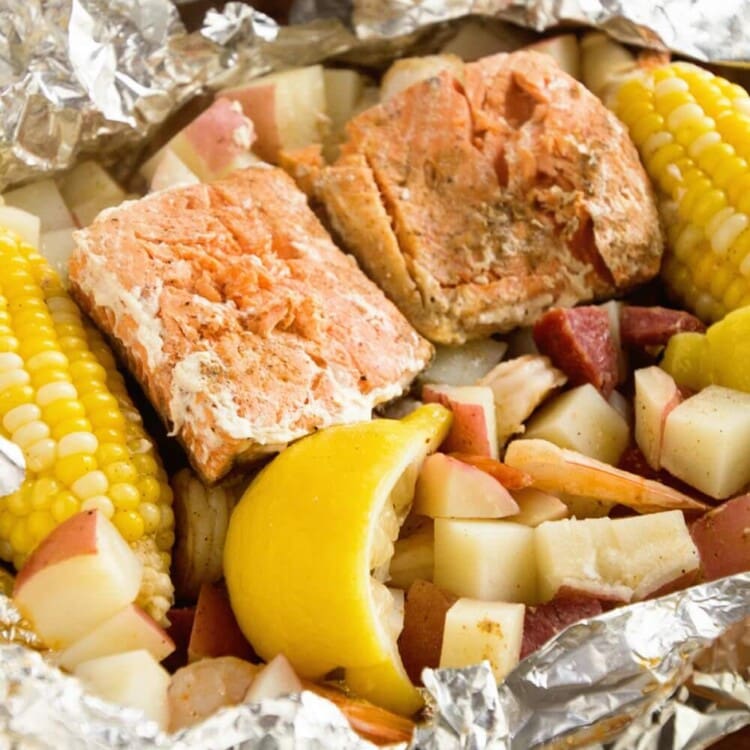 A foil packet of cajun shrimp boil including potatoes, corn on the cob, fish, and lemons