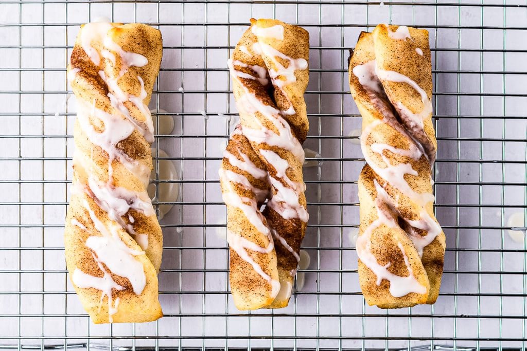 Overhead image of three cinnamon twist with icing on baking rack and white background