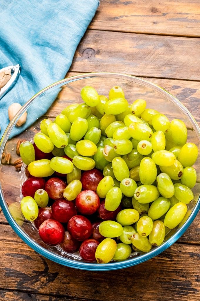 Glass bowl with red and green grapes on a wood background with blue napkin in background