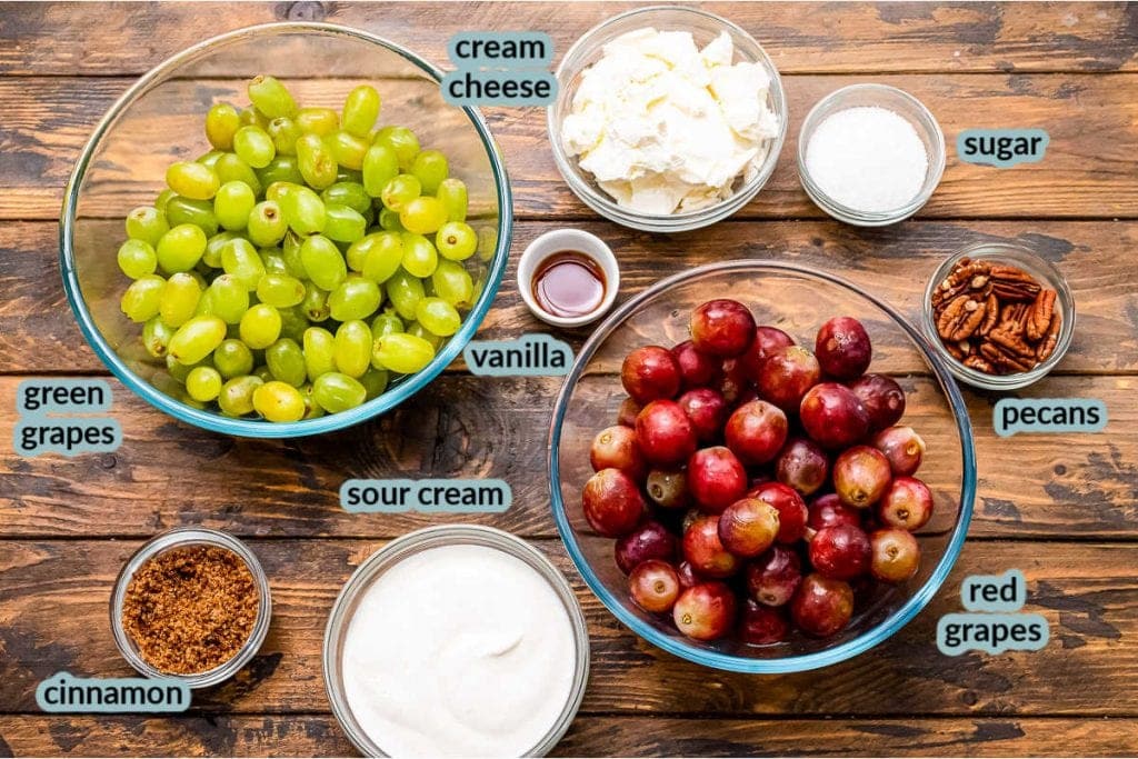 Ingredients in glass bowls on wood background for grape salad. Bowls of red grapes, green grapes, cream cheese, sour cream, brown sugar, pecans, vanilla etc.