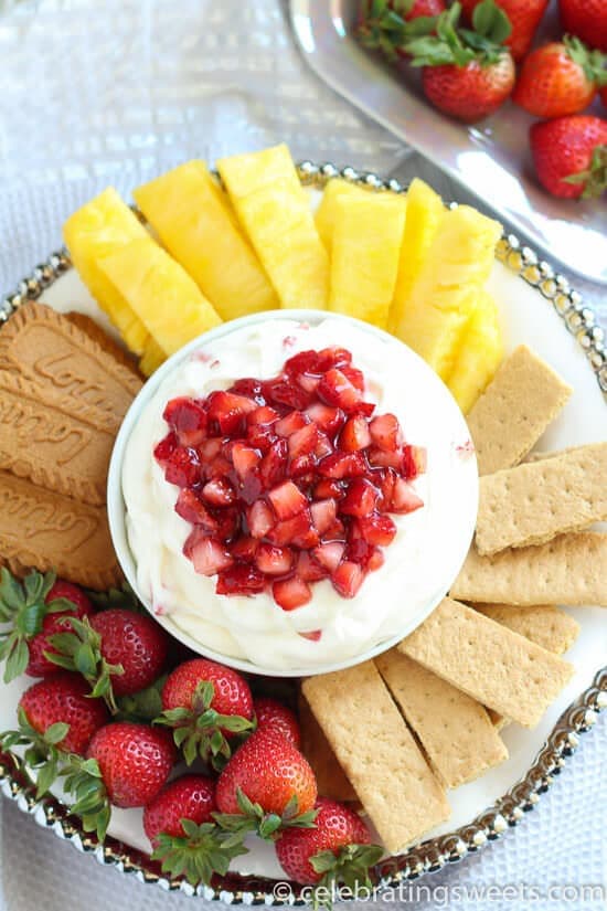 A platter with strawberries pineapple graham crackers and strawberry fruit dip in a bowl in the middle