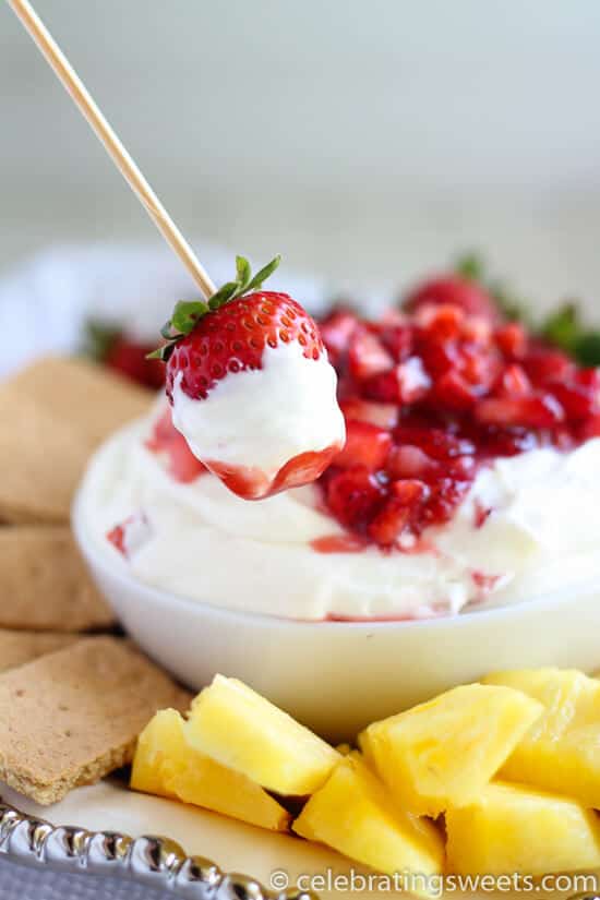 Strawberry on wooden skewer with fruit dip on it a bowl of fruit dip in background with dippers