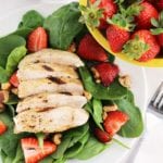Strawberry and balsamic grilled chicken salad on a white plate next to a yellow bowl of strawberries