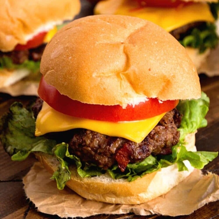 Three whiskey cheddar burgers on parchment paper sitting on a wood table