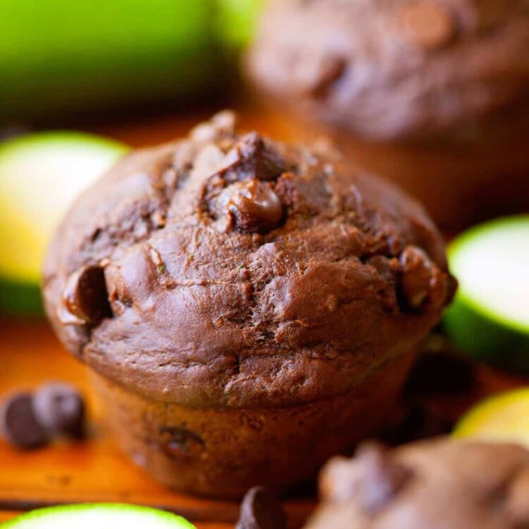 Double chocolate zucchini muffins on a wood table with chocolate chips and zucchini slices