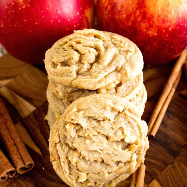 Two stacks of apple peanut butter cookies on a wood board with cinnamon sticks and apples