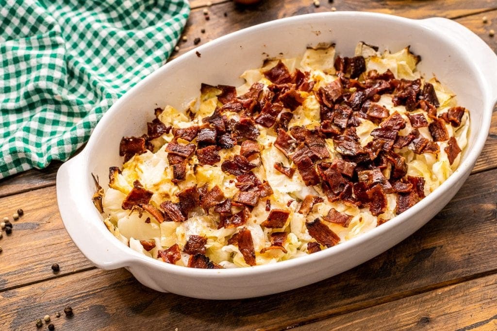 A white baking dish with cooked cabbage casserole in it with green checkered napkin in background