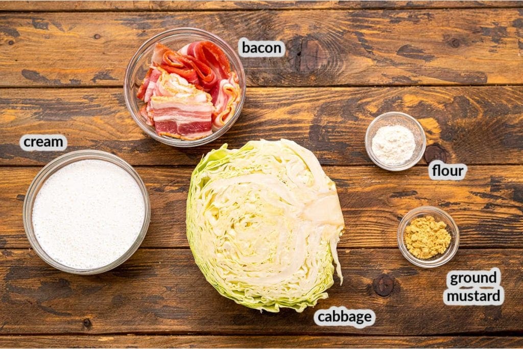 Overhead image of ingredients for cabbage casserole including half head of cabbage, bacon strips, cream, flour and ground mustard in bowls.