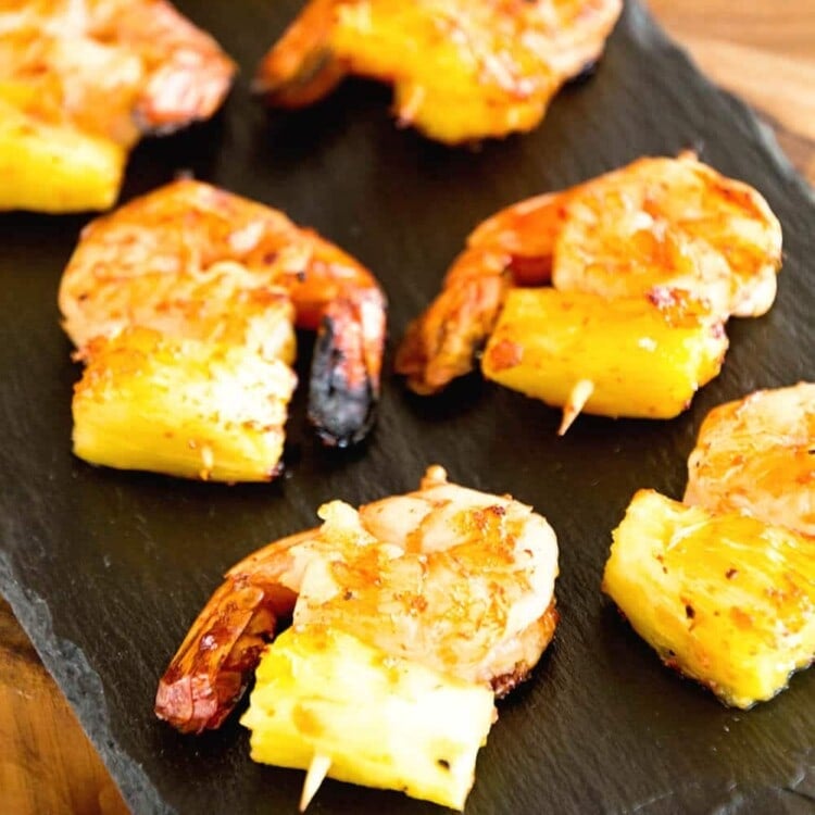 Two rows of grilled bbq pineapple shrimp bites on a slate tray