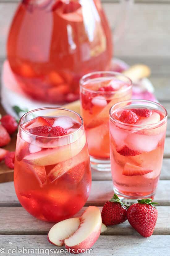 Three glasses full of peach sangria with a pitcher of it in the background