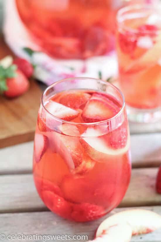 A glass of peach sangria with fresh strawberries, raspberries and sliced peaches in it.