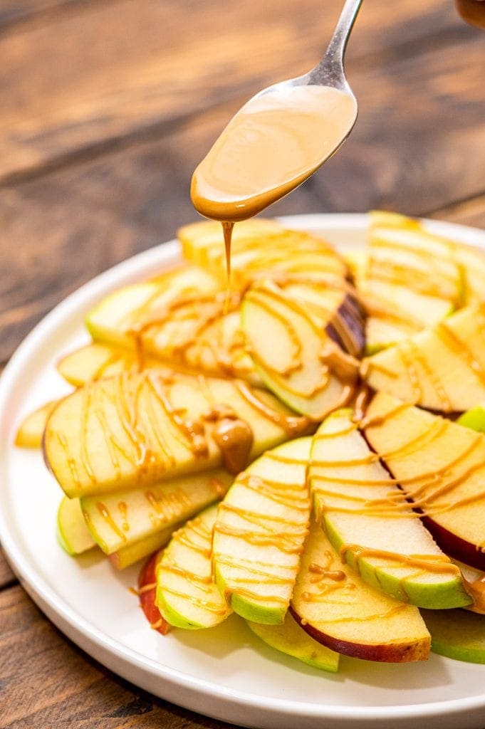 Spoon drizzling peanut butter over the top of thin apple slices