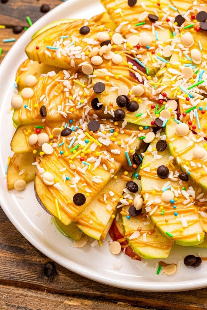 Apple Nachos topped with peanut butter, chocolate chips, coconut and sprinkles. on white plate