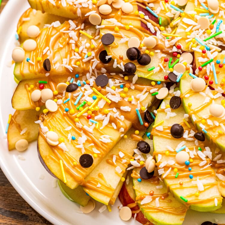 Apple Nachos topped with peanut butter, chocolate chips, coconut and sprinkles. on white plate