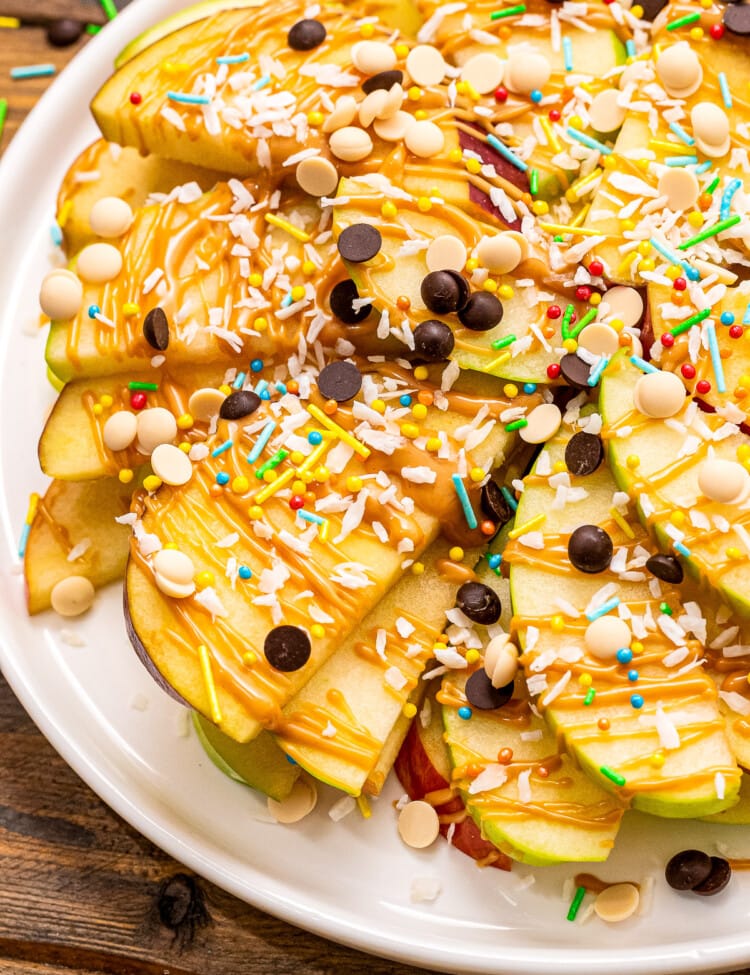 Apple Nachos topped with peanut butter, chocolate chips, coconut and sprinkles. on white plate