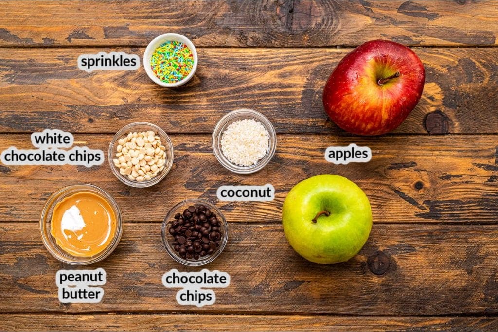 Overhead image of apple nachos ingredients including apples, peanut butter, chocolate chips, coconut and sprinkles in glass bowls.