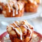 A cinnamon roll monkey bread muffin with icing on a decorative red and gold plate sitting on a marble counter