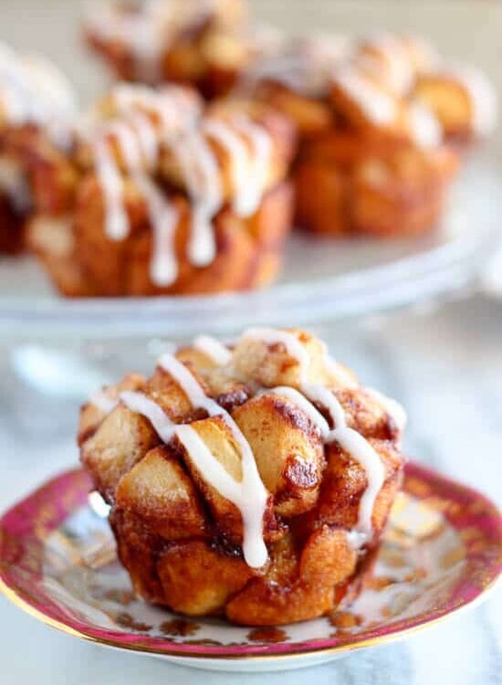 A cinnamon roll monkey bread muffin with icing on a decorative red and gold plate sitting on a marble counter