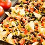 Southwestern nachos with chipotle sauce on a baking sheet topped with tomato, olives, and corn