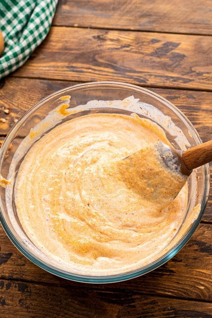 Spatula mixing pumpkin filling for cake in a glass bowl.