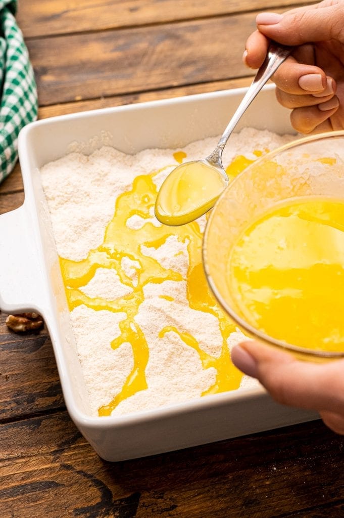 A hand pouring butter of cake mix out of a spoon.