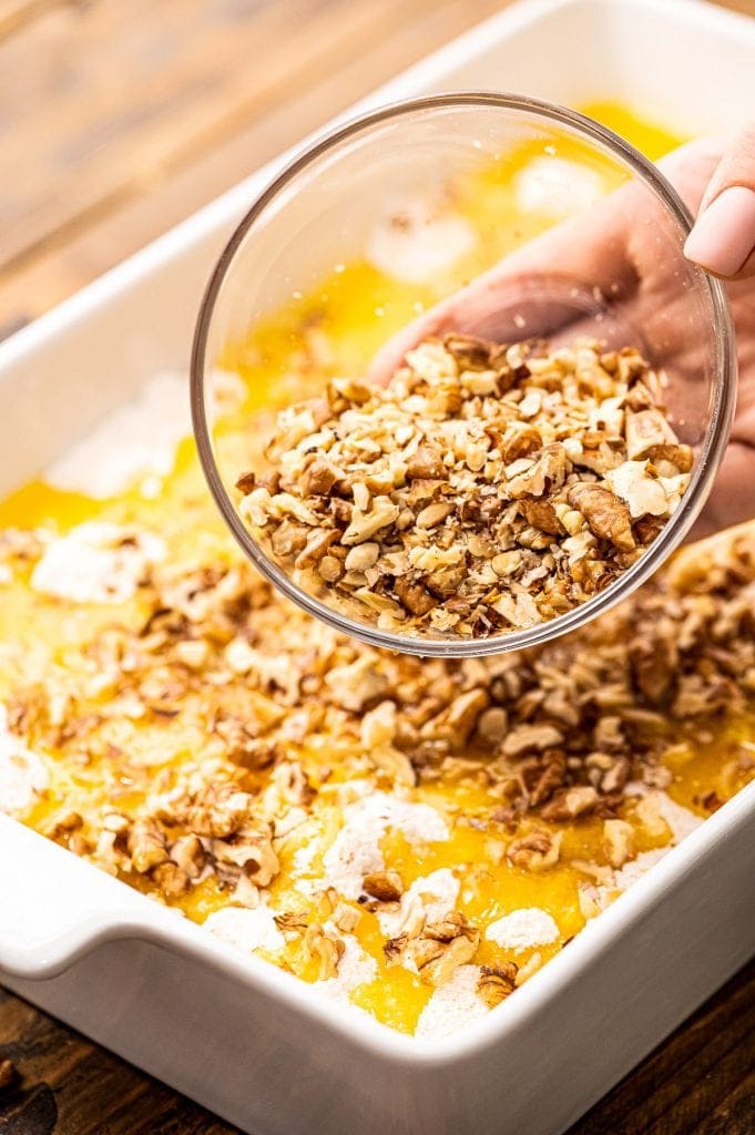 Hand pouring chopped walnuts on top of cake before baking