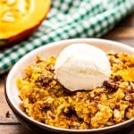 Pumpkin Dump Cake in a bowl with a scoop of ice cream on top. A green and white checkered napkin behind it.