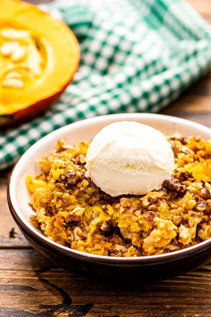 Pumpkin Dump Cake in a bowl with a scoop of ice cream on top. A green and white checkered napkin behind it. 