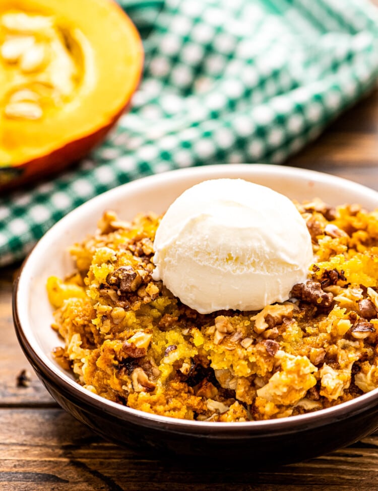 Pumpkin Dump Cake in a bowl with a scoop of ice cream on top. A green and white checkered napkin behind it.