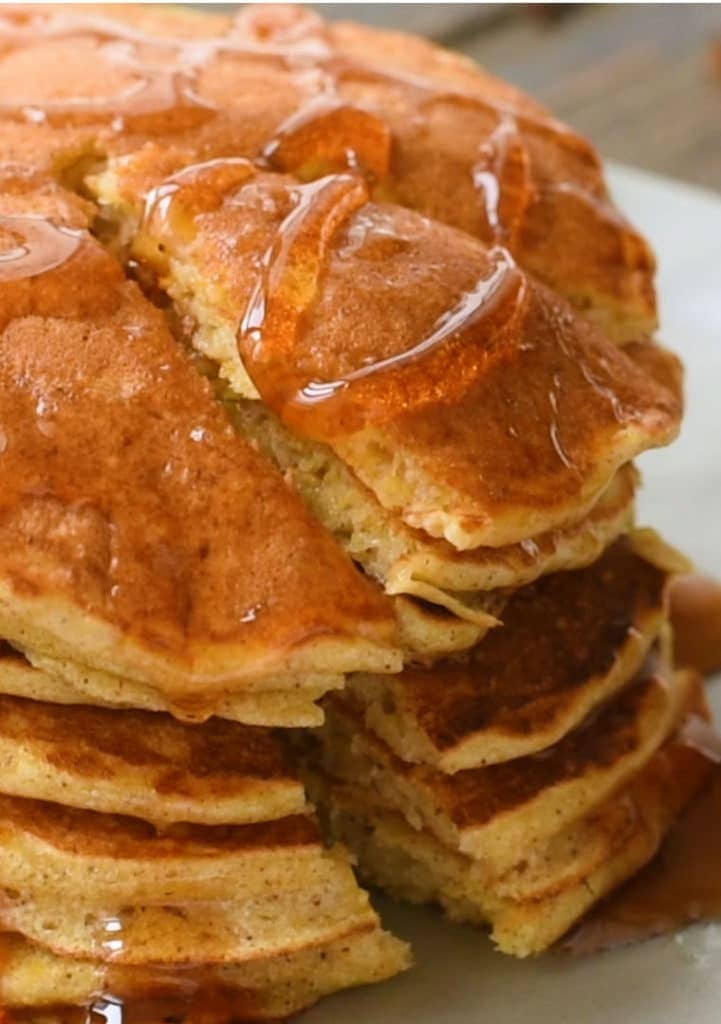 Stack of pumpkin pancakes with maple syrup. On triangle cut into them to take a bite.