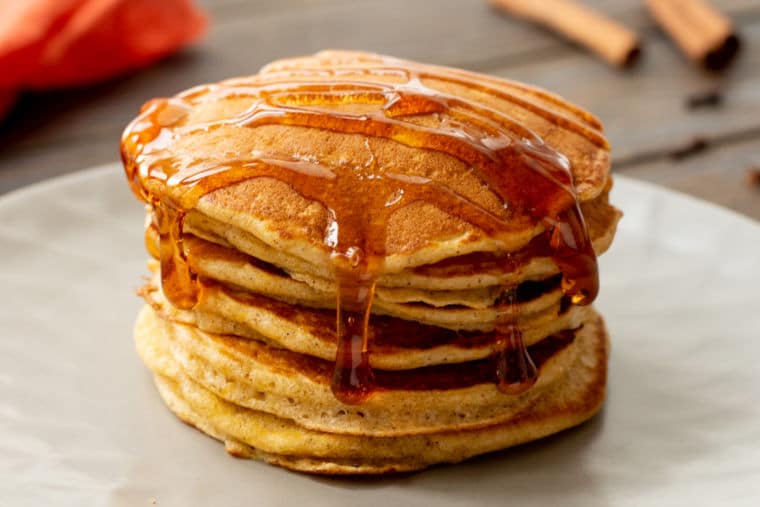 Stack of pumpkin pancakes drizzled with syrup on white plate.