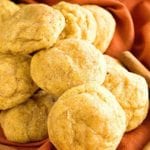 A pile of pumpkin snickerdoodle cookies on an orange cloth napkin with cinnamon sticks