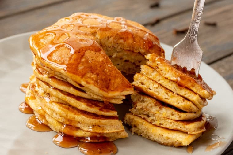 Fork stabbing a bite of pumpkin pancakes with the rest of the pancakes sitting on the white plate.