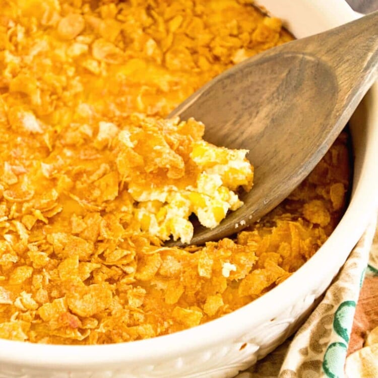 A white bowl of corn pudding casserole with a wooden spoon