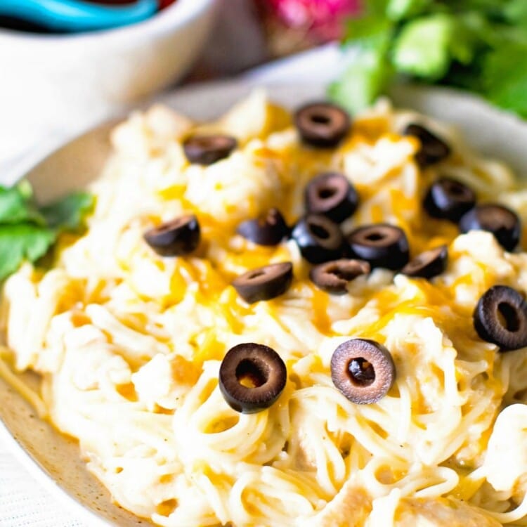 Pasta with chicken topped with black olives on a white plate