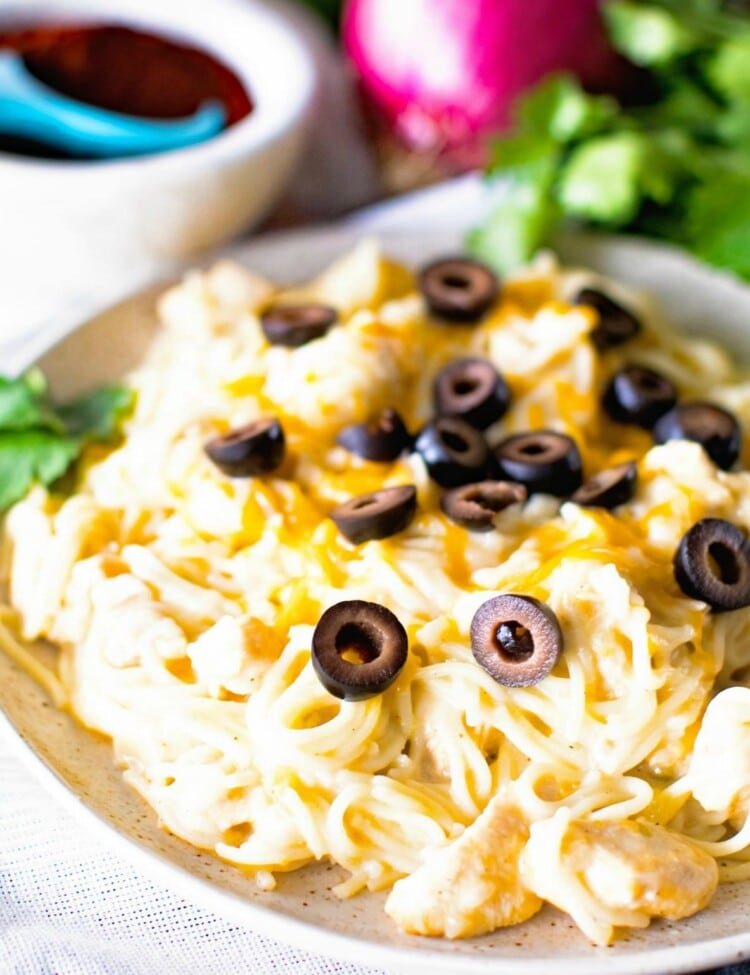 Pasta with chicken topped with black olives on a white plate