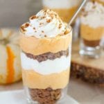 A small glass of pumpkin cream pie trifle topped with whipped cream and with a little spoon in it