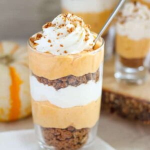 A small glass of pumpkin cream pie trifle topped with whipped cream and with a little spoon in it